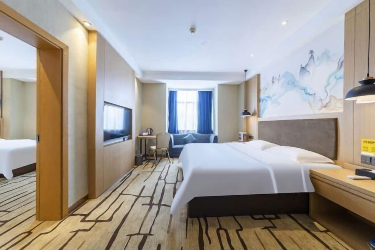 A hotel room with a large bed, a desk, a chair, a TV, and a window with curtains.