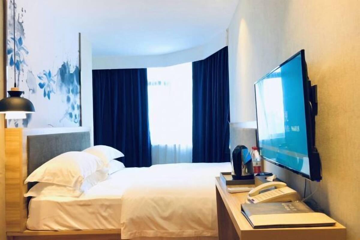 A hotel room with a bed, a desk with a telephone, a flat-screen TV, and a painting on the wall.