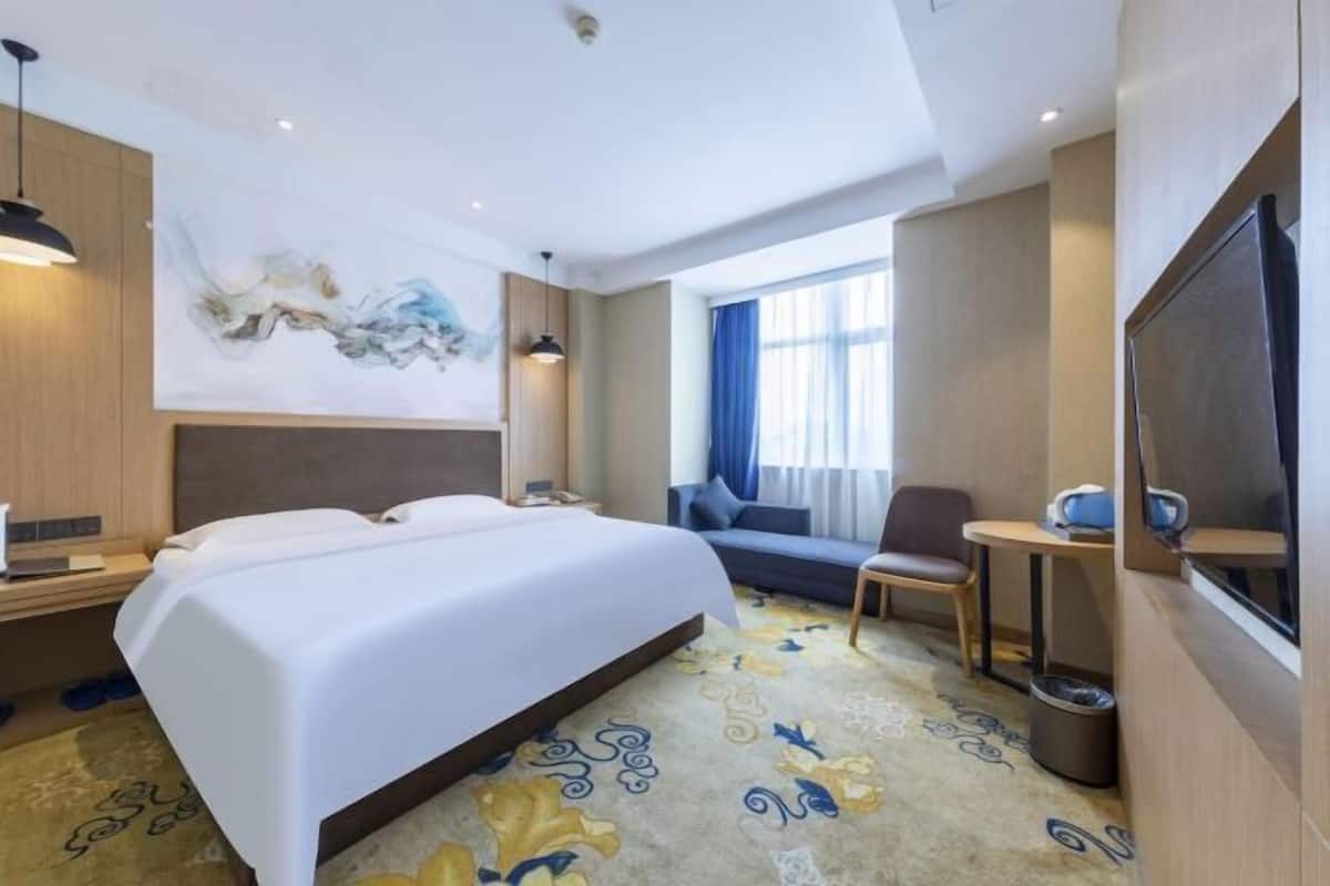 A hotel room with a bed, a sofa, a TV, a desk, and a painting on the wall.