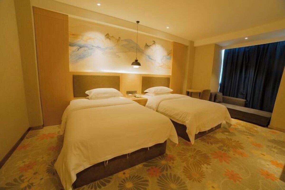 A hotel room with two beds, a mural on the wall, a nightstand, and a window with curtains.