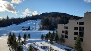 A snow-covered ski slope with a lodge, a building with multiple windows, and a forested hill in the background. - Ride and Relax Snowshoe Vacation Rental (Pocahontas County)