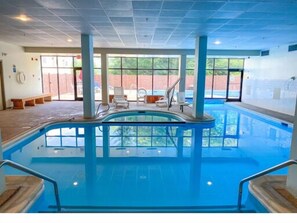 An indoor swimming pool with clear glass walls, a tiled floor, and a few lounge chairs. - Ride and Relax Snowshoe Vacation Rental (Pocahontas County)