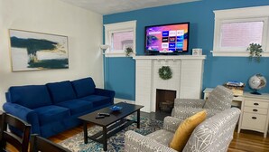 Ein Wohnzimmer mit blauem Sofa, einem gemusterten Sessel und einem Kamin mit Adventskranz.