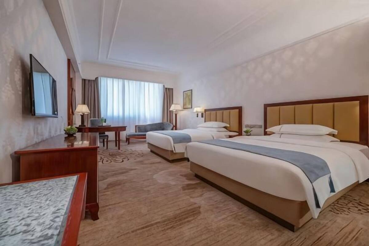 Une chambre d’hôtel avec deux lits, un bureau, une chaise, une télévision et une fenêtre avec des rideaux.