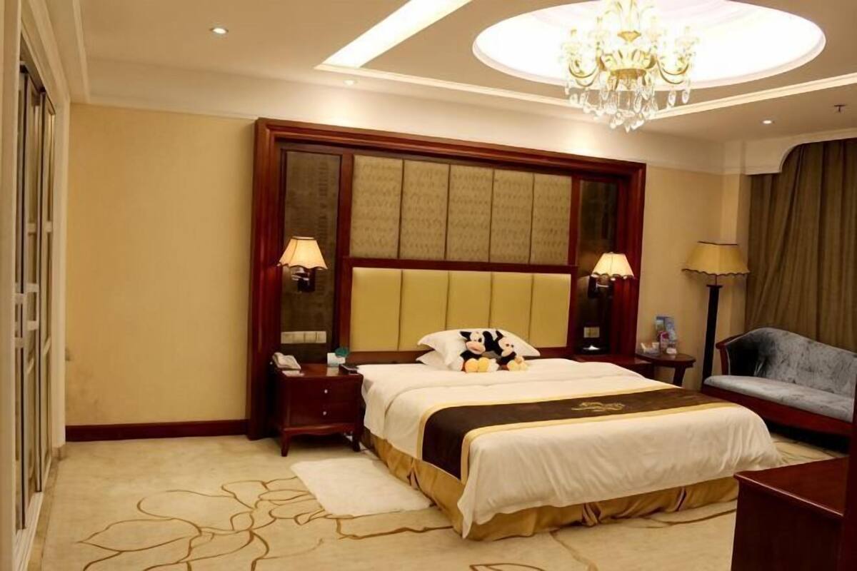 Une chambre d’hôtel avec un grand lit, des lampes de chevet, un bureau, une chaise et un lustre.