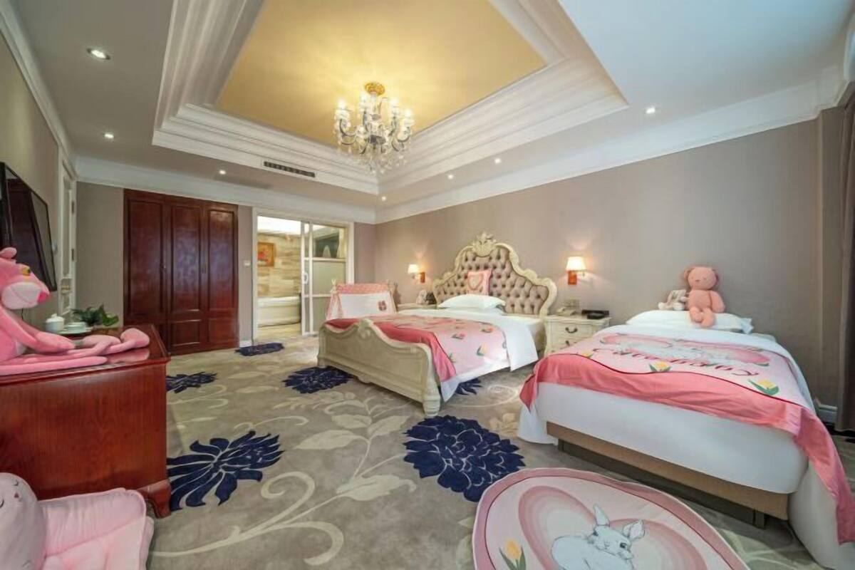 Une chambre d’hôtel avec un grand lit, un lit plus petit, un bureau, une chaise et un lustre.