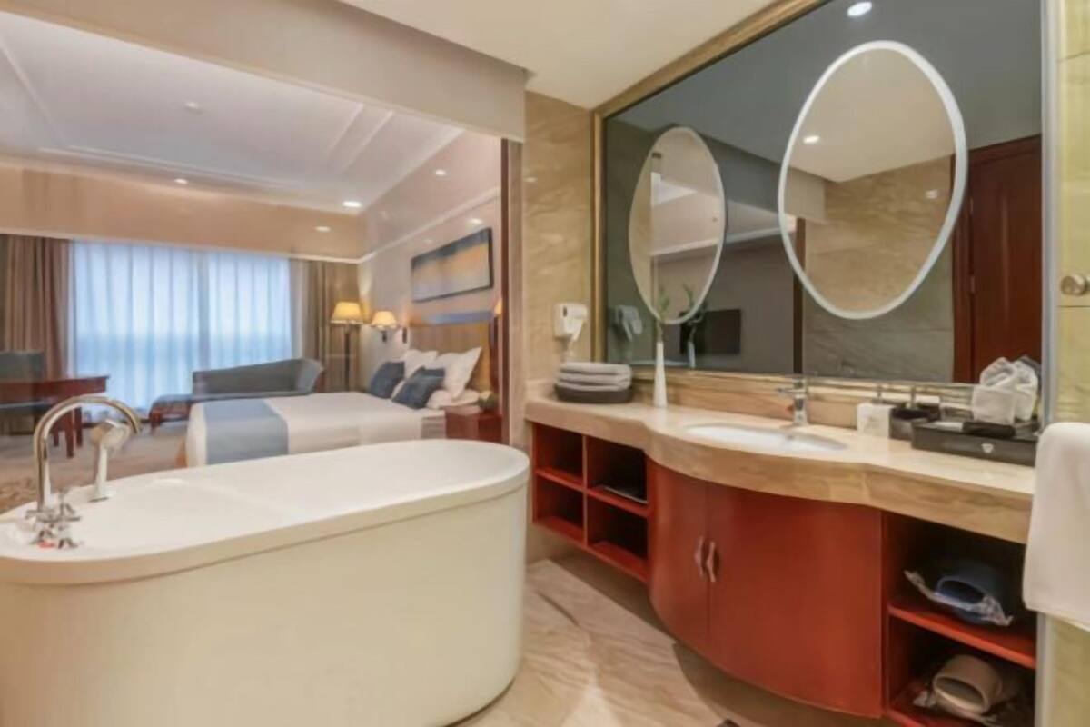 Une chambre d’hôtel moderne dotée d’une grande baignoire, d’une douche séparée, d’un grand miroir et d’un lit offrant une vue sur la ville.