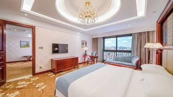 A hotel room with a large bed, a desk, a television, and a balcony with a view.