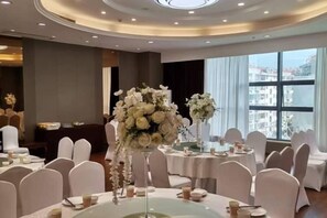 A banquet hall with round tables, white chairs, and floral centerpieces. - Dong Zheng International Hotel (Hechi)