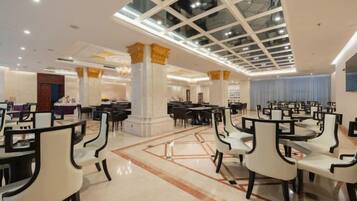 A spacious dining area with multiple tables and chairs, a high ceiling with a skylight, and decorative columns.