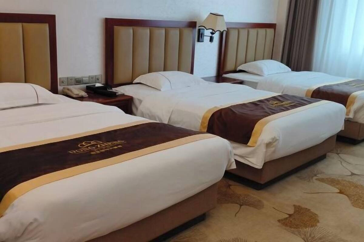Une chambre d’hôtel avec trois lits, une table de chevet, une lampe et un téléphone.