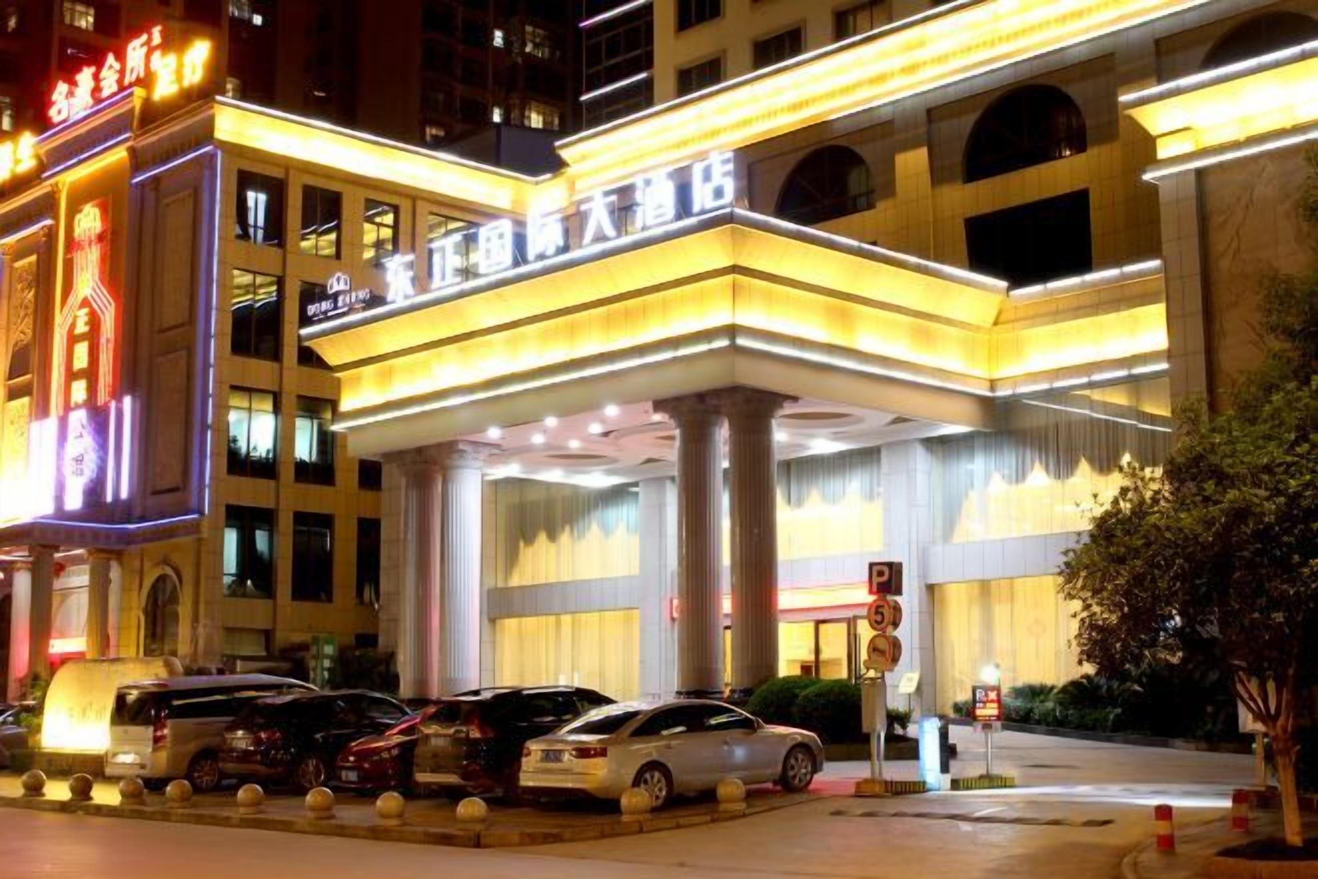 A hotel entrance with a large canopy, multiple floors, and parked cars.