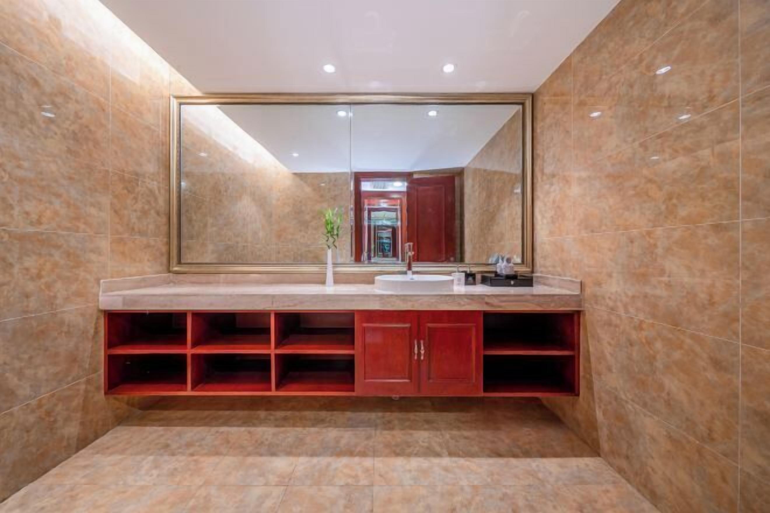 A modern bathroom with a large mirror, marble tiles, and a red cabinet.