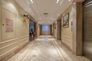 Un pasillo de hotel con suelo de mármol, lámparas en la pared y una puerta con un cartel.