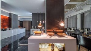 A modern hotel lobby with a central breakfast bar, a seating area with tables and chairs, and a large mirror reflecting the space. - Dong Zheng International Hotel (Hechi)