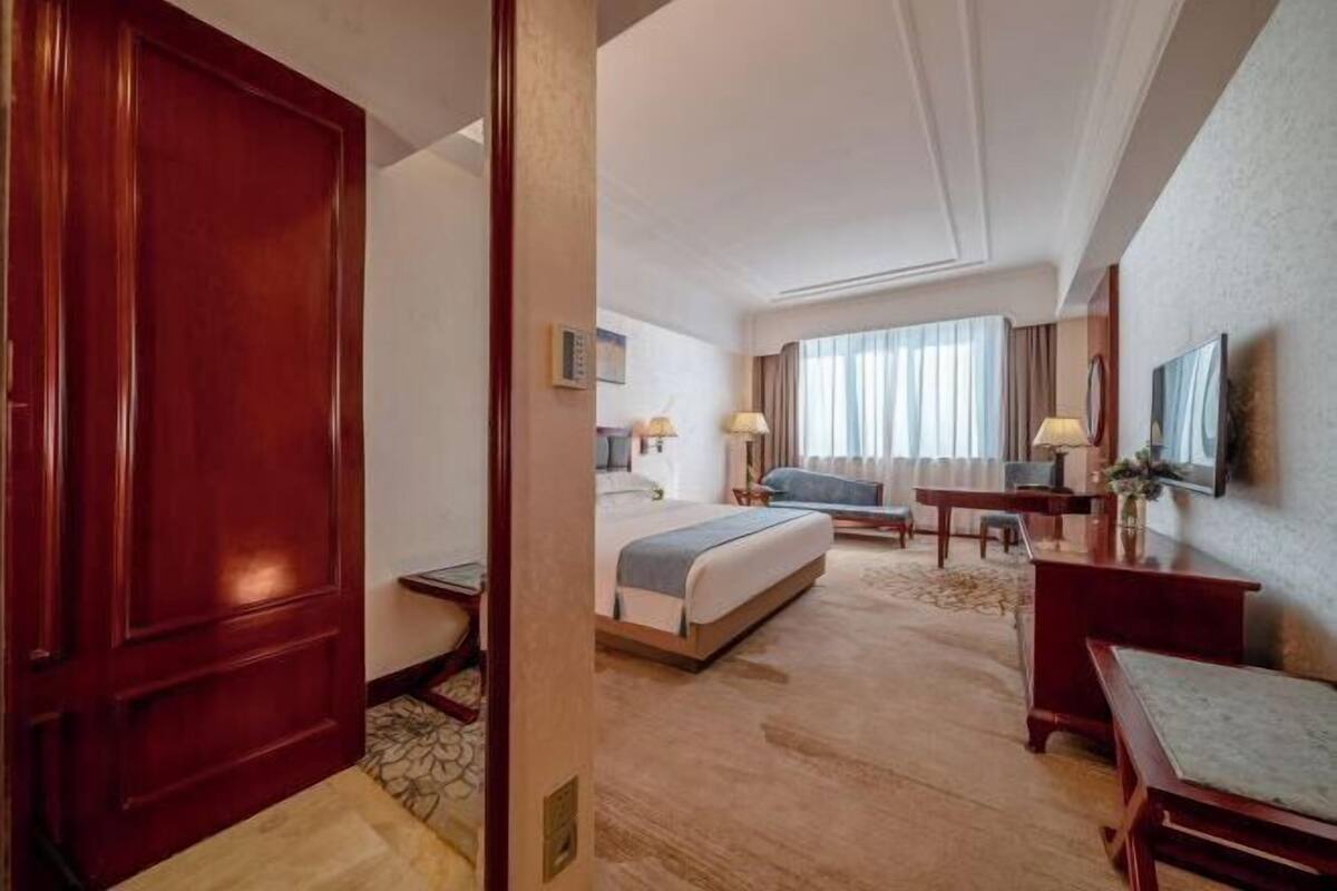 Une chambre d’hôtel avec un lit, un bureau, une chaise, une télévision et une fenêtre avec des rideaux.
