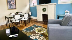 A living room with a white fireplace, blue walls, a dining table with chairs, a grey sofa, and a patterned rug.