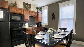 Una cocina moderna con armarios de madera, un refrigerador negro y una mesa de comedor preparada para cuatro comensales.