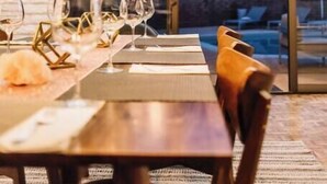Een eethoek met een tafel voor vier personen, een grote hanglamp en uitzicht op een bergachtig landschap door een glazen deur.