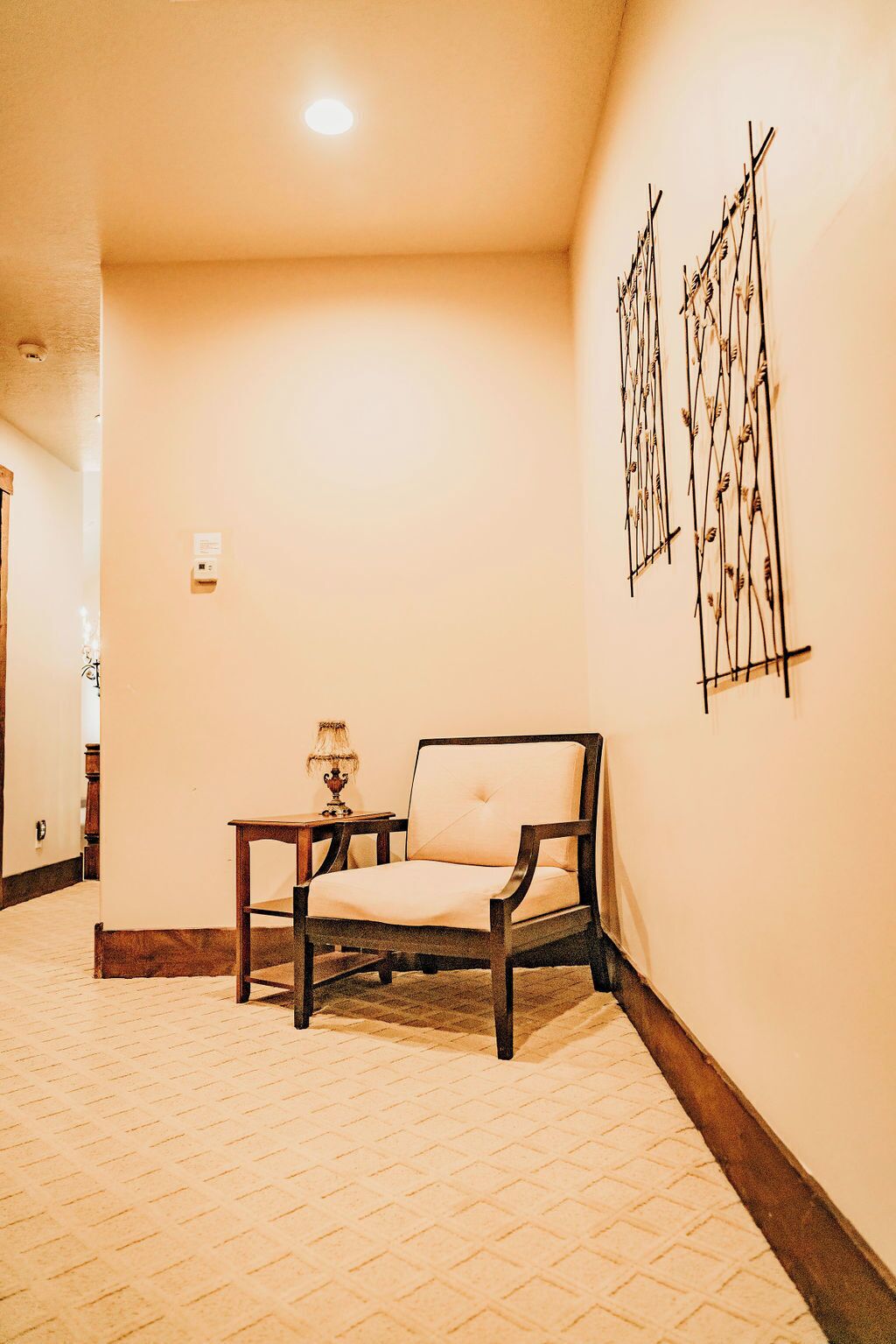 A hallway with a wooden chair and a small table, a wall-mounted artwork, and a door at the end.