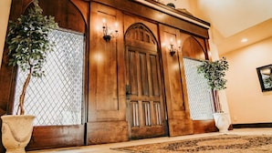 Une imposante porte d’entrée en bois, dotée d’un grand portail en arc de cercle, flanquée de deux plantes en pot et agrémentée d’appliques murales.
