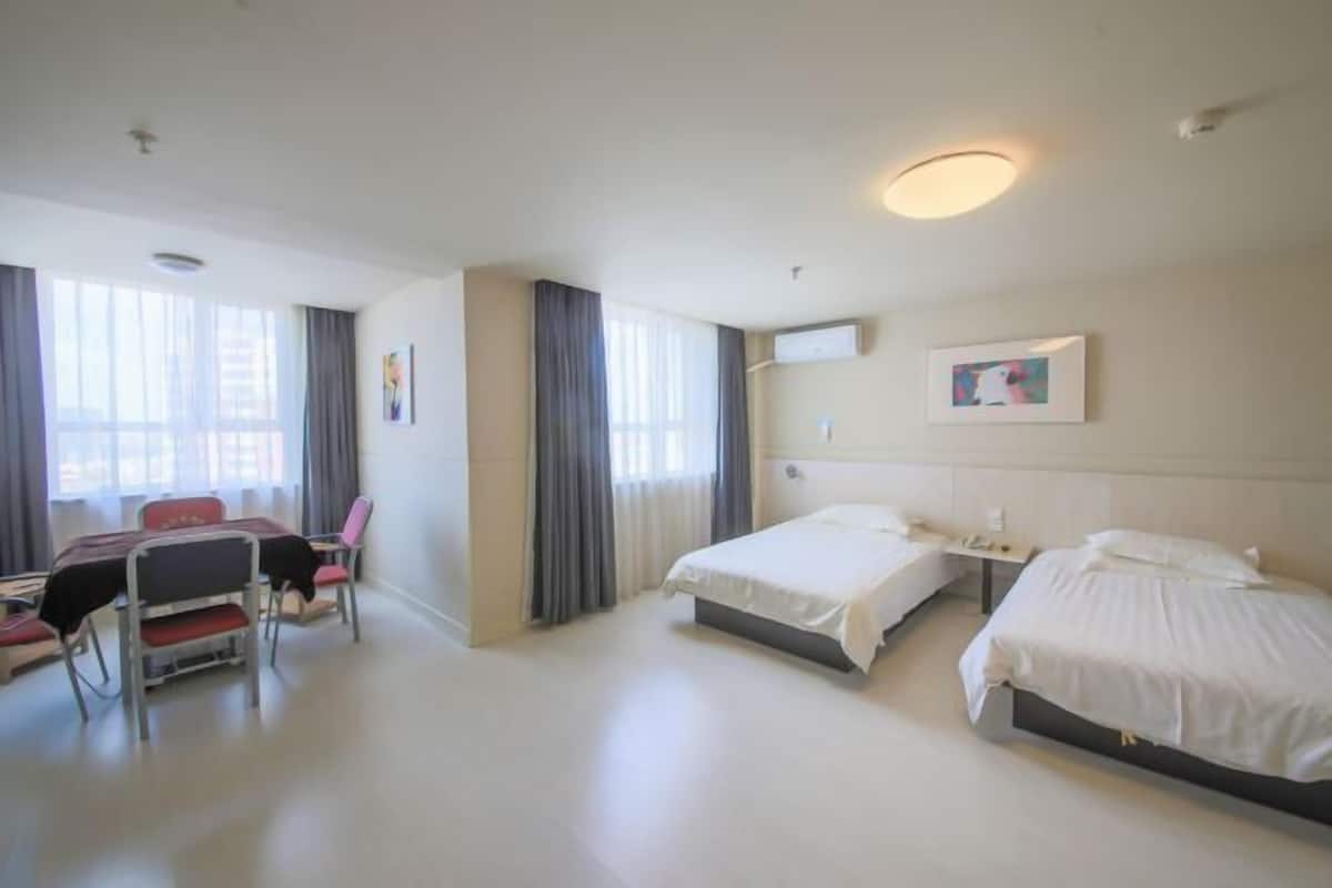 Hotellihuone, jossa on kaksi sänkyä, työpöytä tuolilla sekä suuri ikkuna, jossa on verhot.