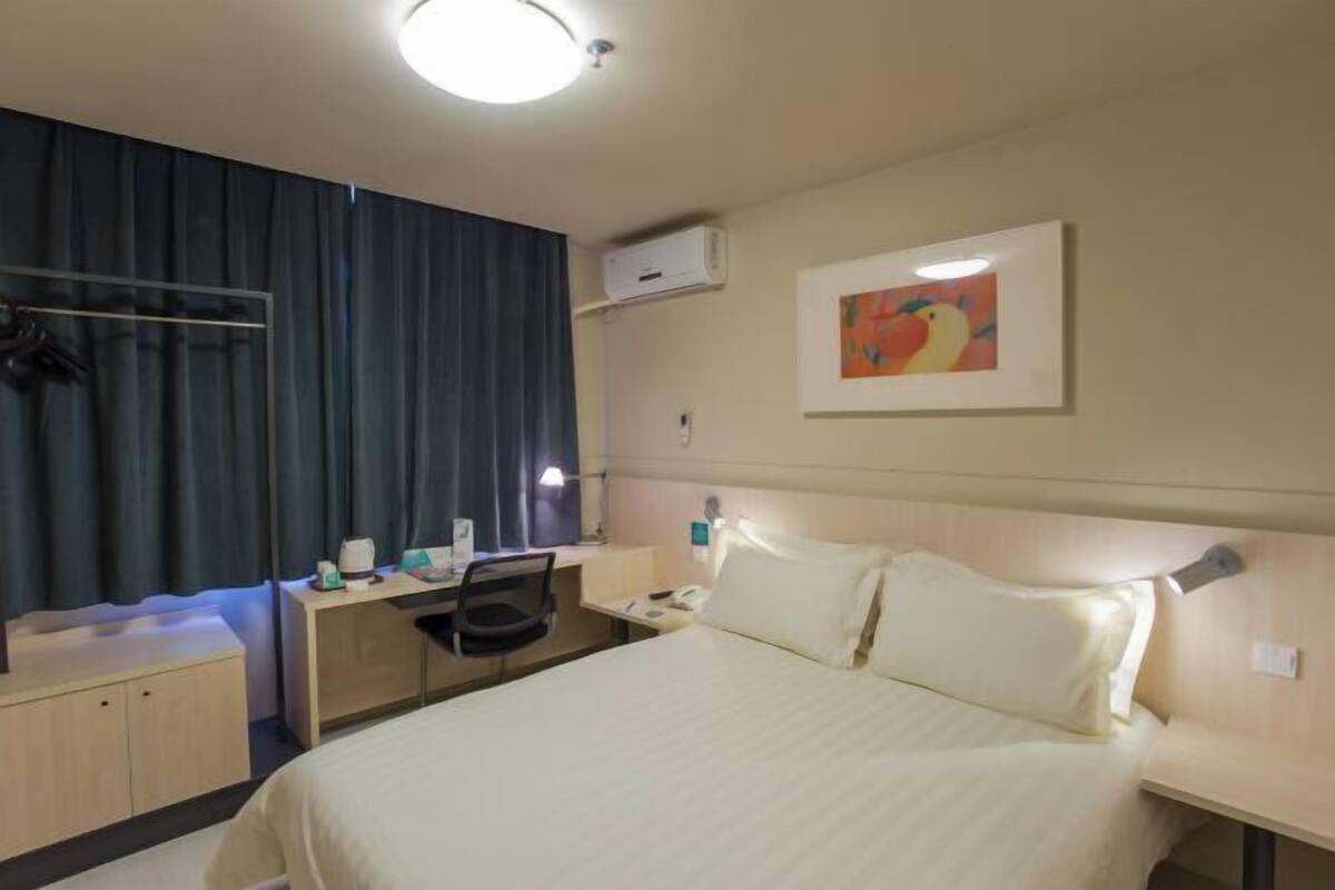 Hotellihuone, jossa on sänky, työpöytä, tuoli ja taulu seinällä.