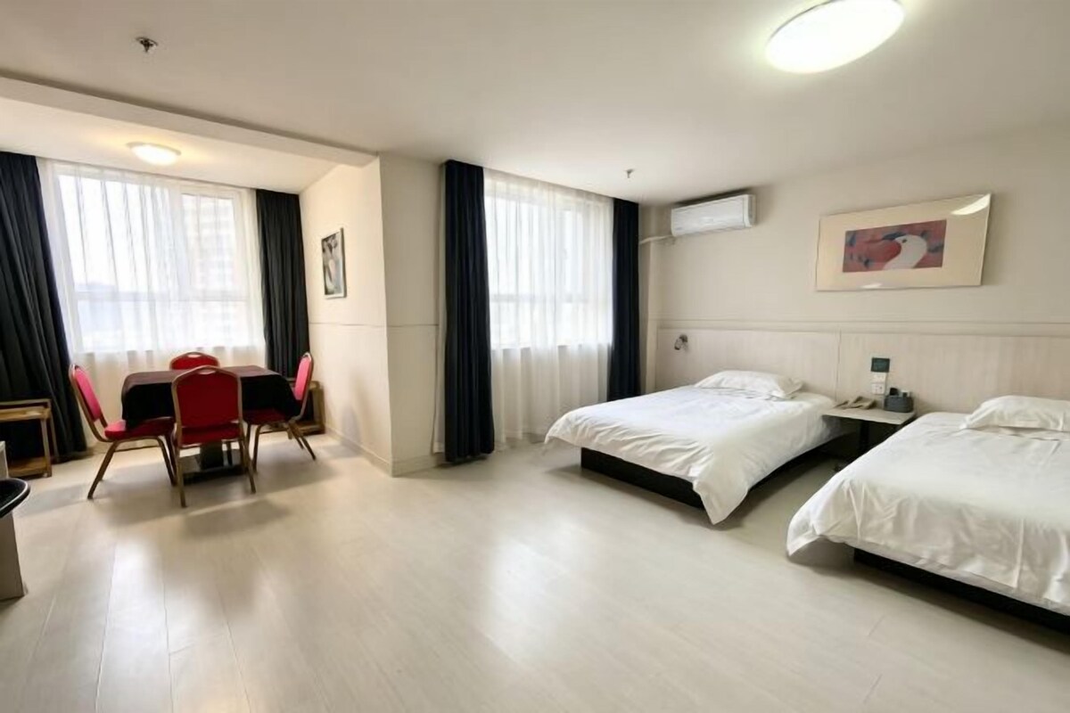 A hotel room with two beds, a dining table with chairs, and a large window with curtains.