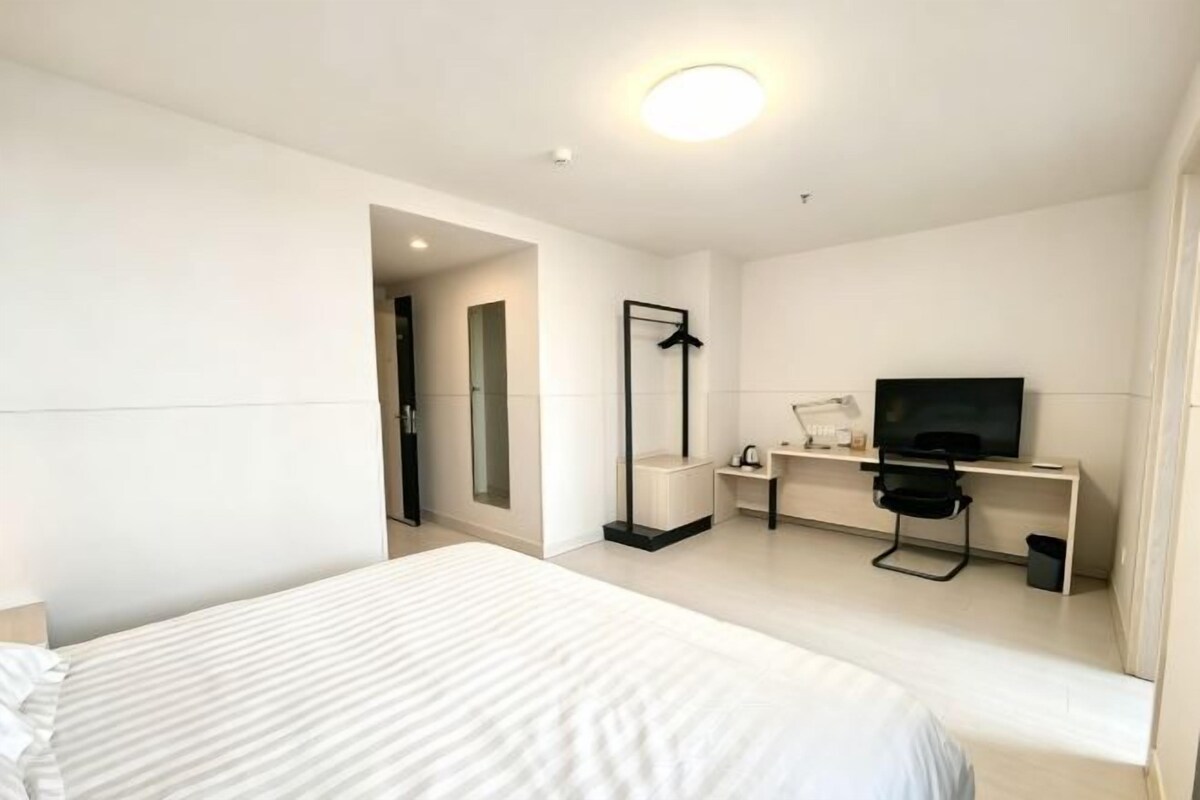 A hotel room with a bed, a TV, a desk, and a mirror.