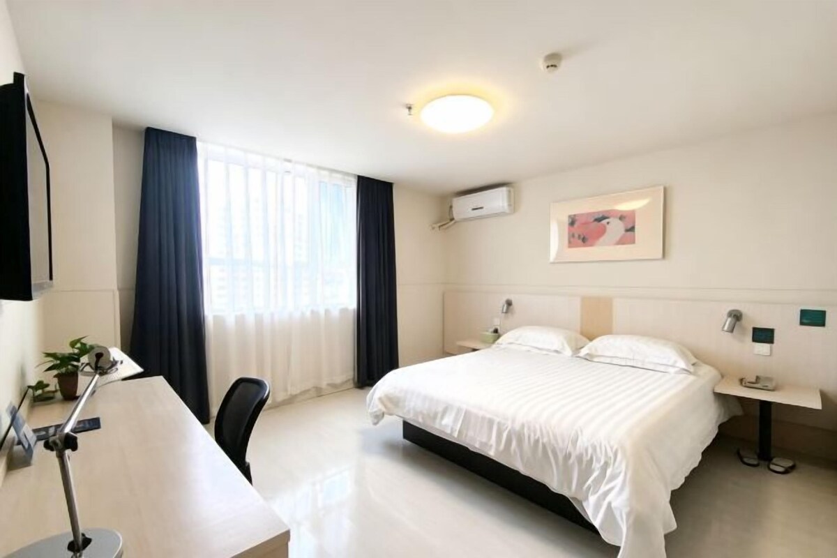 A hotel room with a bed, desk, chair, and a window with curtains.