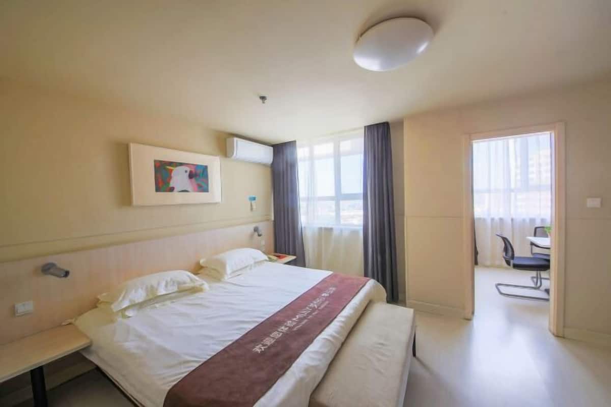 Hotellihuone, jossa on sänky, yöpöytä, taulu seinällä, ikkuna verhoilla ja näkymä ulos.