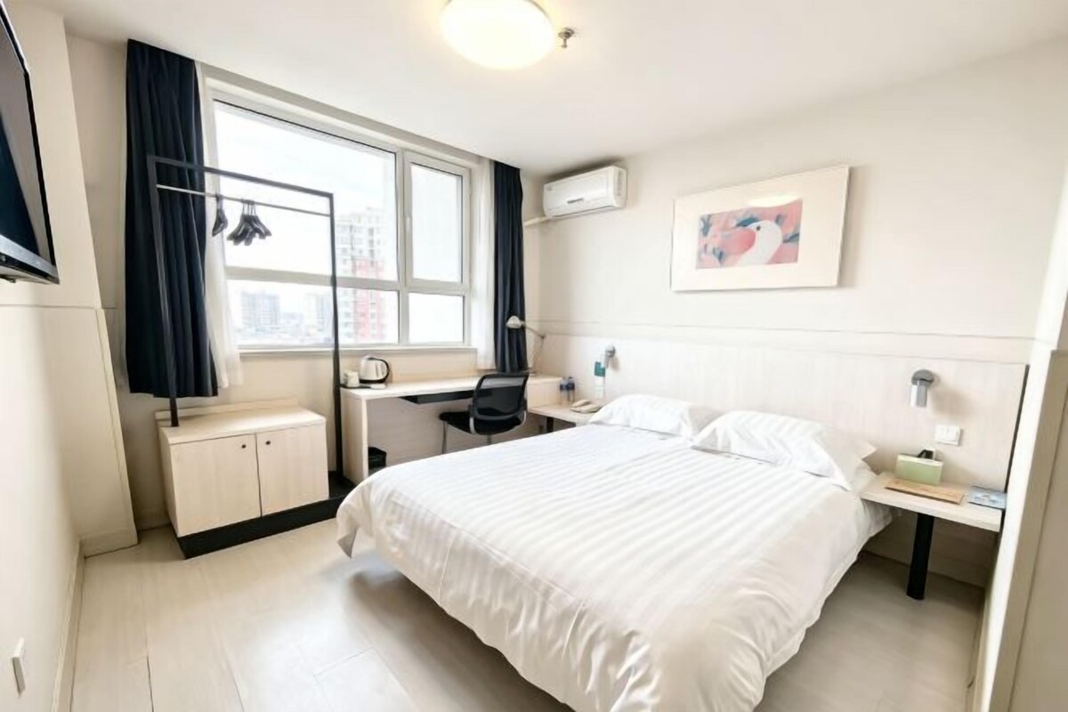 A hotel room with a bed, desk, chair, and a window with curtains.