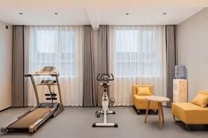 A hotel room with a treadmill, exercise bike, two yellow chairs, a small table, and a water dispenser. - Jinjiang Inn (Ulanqab Jining Railway Station Xingfu Road) (Ulanqab)
