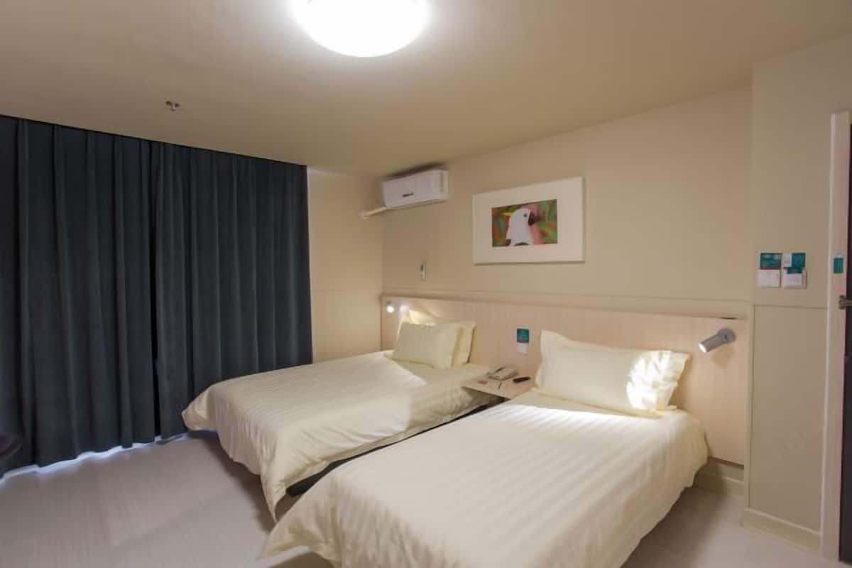 Hotellihuone, jossa on kaksi sänkyä, kattovalaisin, taulu seinällä ja ovi, jossa on kahva.