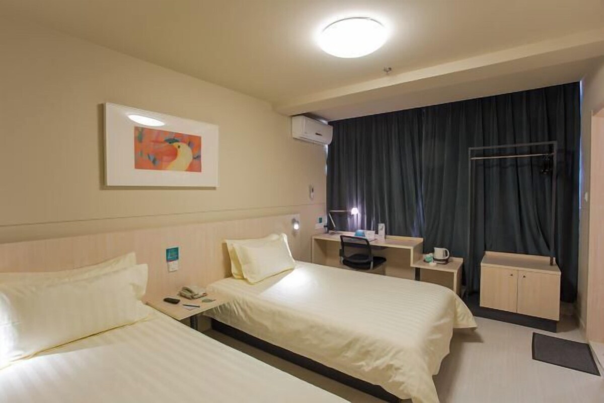 Habitación de hotel con dos camas, un escritorio, una silla, una computadora, un teléfono y una ventana con cortinas.