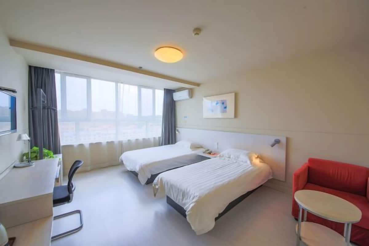 Hotellihuone, jossa on kaksi sänkyä, työpöytä, tuoli, punainen sohva ja ikkuna, jossa on verhot.