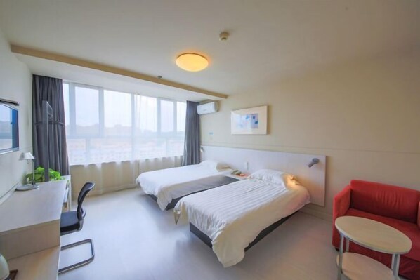 Ein Hotelzimmer mit zwei Betten, einem Schreibtisch, einem Stuhl, einem roten Sofa und einem Fenster mit Vorhängen.