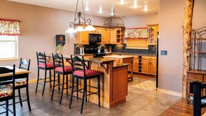 A kitchen with wooden cabinets, a central island, bar stools, and pendant lighting. - Lake Vista Lodge | 5BR Sleeps 24 | Stunning Lake Views, Direct ATV & Snowmobile Trail Access (Garden City)