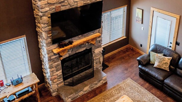 A living room with a stone fireplace, a flat-screen TV, a leather sofa, and a coffee table. - Lake Vista Lodge | 5BR Sleeps 24 | Stunning Lake Views, Direct ATV & Snowmobile Trail Access (Garden City)