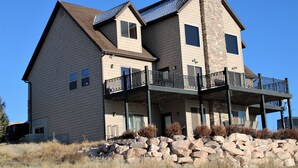 A two-story house with a stone chimney, a balcony with a railing, and a stone foundation. - Lake Vista Lodge | 5BR Sleeps 24 | Stunning Lake Views, Direct ATV & Snowmobile Trail Access (Garden City)