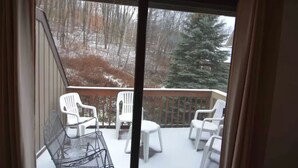 A balcony with white plastic chairs and a metal chair, overlooking a snowy landscape with trees and a large evergreen. - Peek' n Peak, Camelot  Loft Condo,  Clymer, NY, 250 Yards to Chair 8, Sleeps 14 (Clymer)