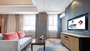 A hotel room with a sofa, a coffee table, a TV mounted on the wall, and a patterned carpet. - Lingyu International Boutique Hotel (Jinghe)