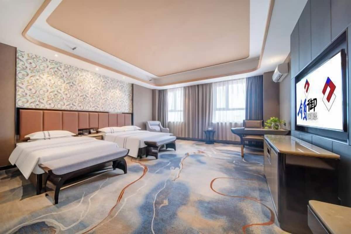 Ein Hotelzimmer mit zwei Betten, einem Schreibtisch, einem Fernseher und einer Wand mit Muster.