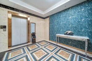 Un ascenseur, un mur de marbre et un sol à motifs dans le hall d’un hôtel.