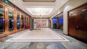 A hotel lobby with a marble floor, a chandelier, a reception desk, and a large painting on the wall.