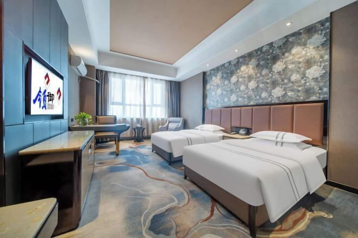 Ein Hotelzimmer mit einem großen Bett, einem Schreibtisch, einem Stuhl, einem Fernseher und einer Wandverzierung.