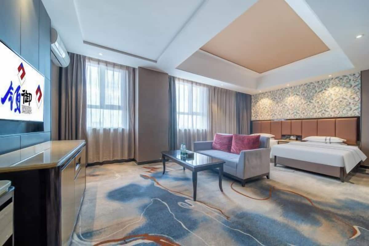 Ein Hotelzimmer mit Bett, Sofa, Couchtisch, Fernseher und einem gemusterten Teppich.