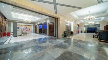A spacious lobby with a marble floor, a reception desk, a chandelier, and a seating area.