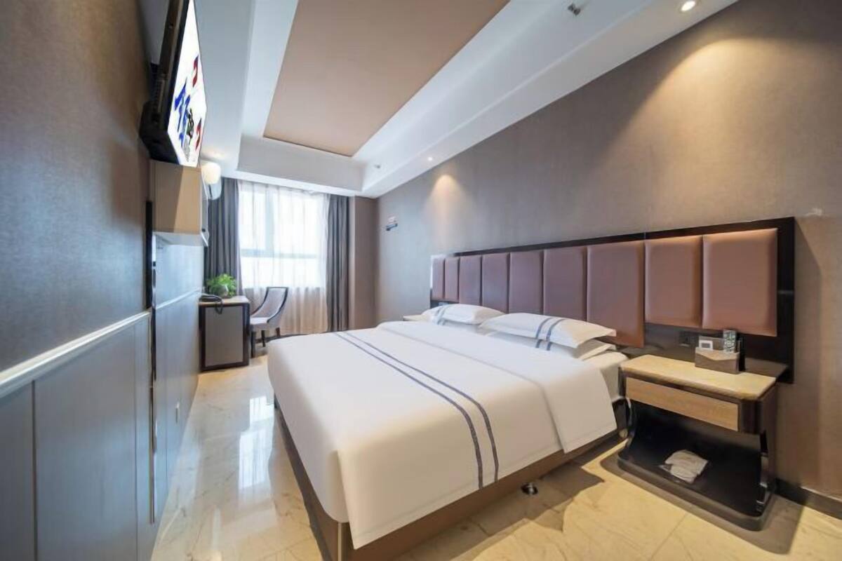 Ein modernes Hotelzimmer mit einem großen Bett, Nachttischen, einem Schreibtisch und einem Fernseher.
