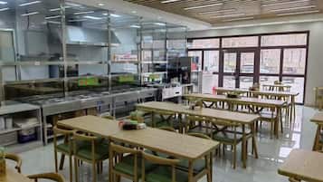 A restaurant with a kitchen area, dining tables, and chairs.